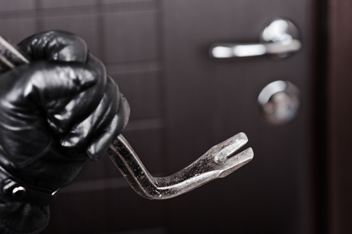 hand with black glove holding a crowbar in front of a door